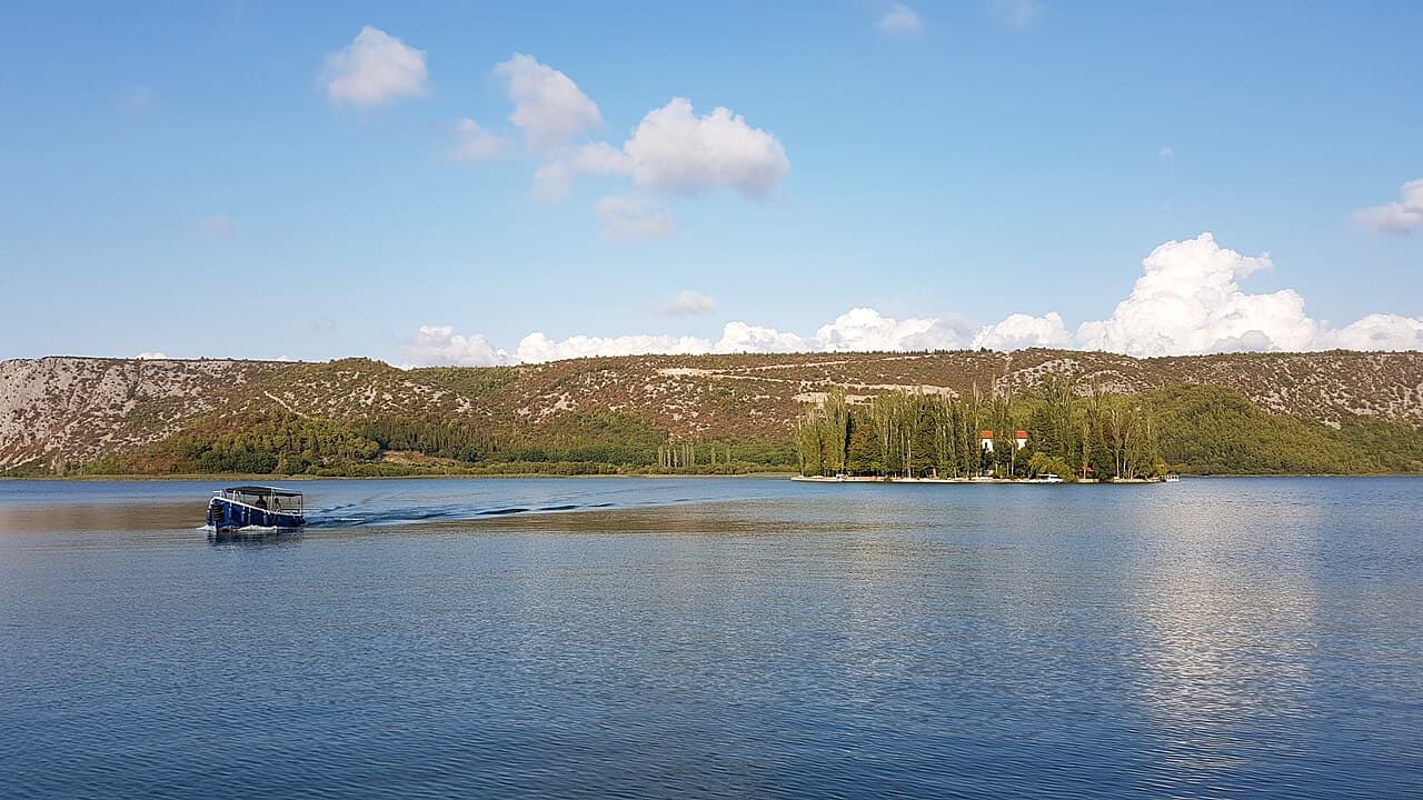 Visovac island in the Krka river lake with a park boat passing